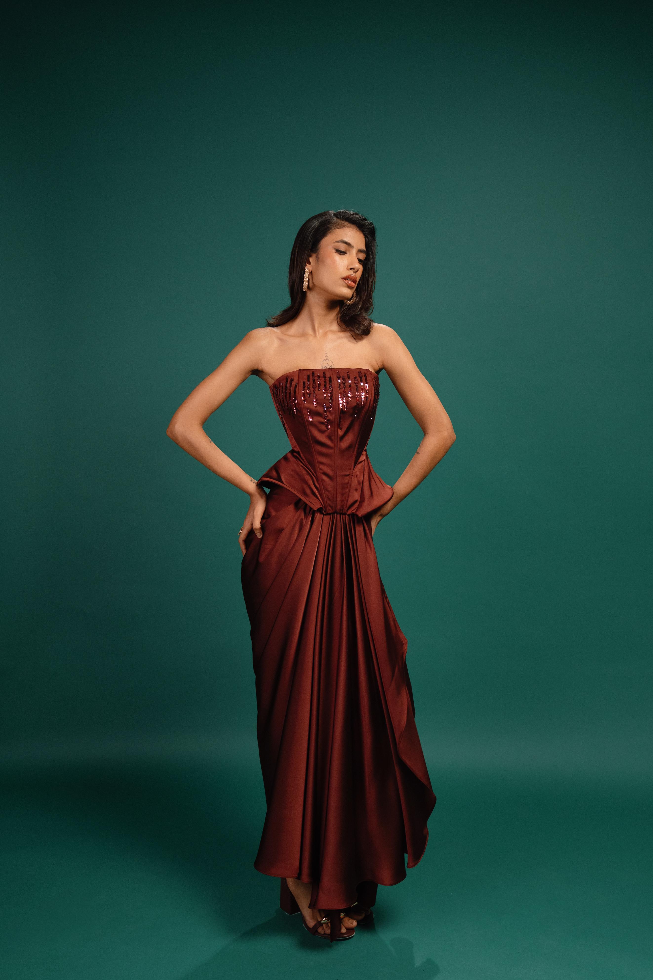 Woman wearing a strapless red evening gown against a teal background